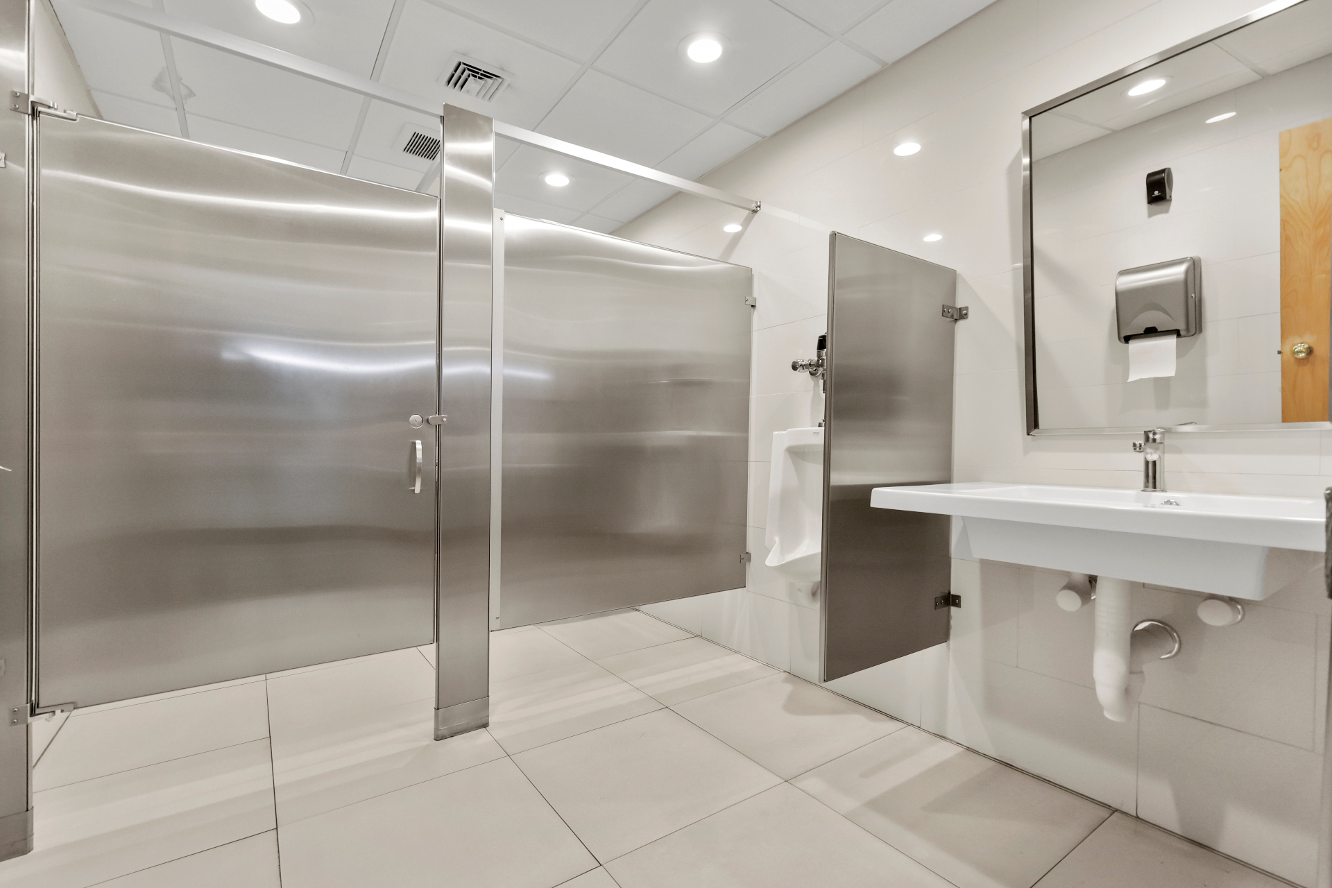 Bright restroom with stainless partitions, large mirror, and new tile